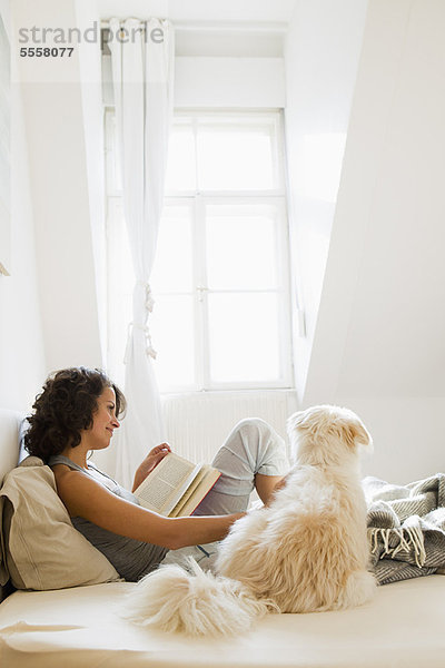 Frau liest im Bett mit Hund