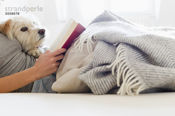 Frau liest im Bett mit Hund