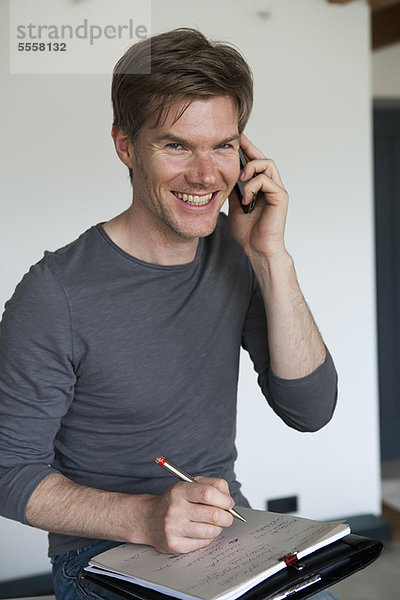 Lächelnder Mann am Handy macht sich Notizen