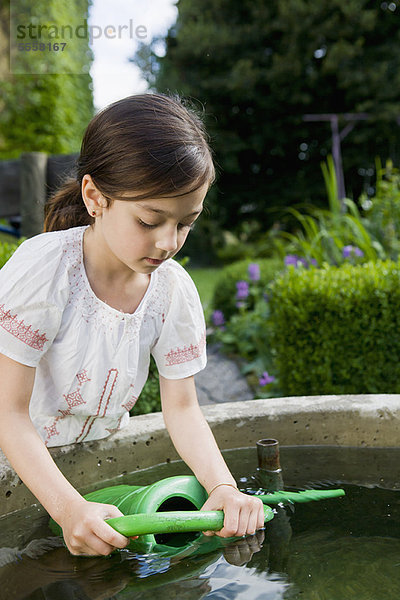 Mädchen beim Auffüllen der Gießkanne im Springbrunnen