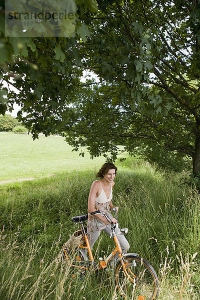 Frau schiebt Fahrrad im hohen Gras