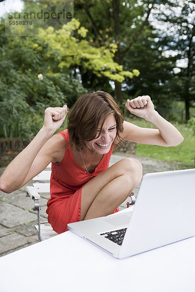 Frau jubelt auf Laptop im Freien