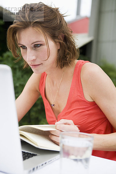 Frau beim Lesen und Benutzen des Laptops im Freien