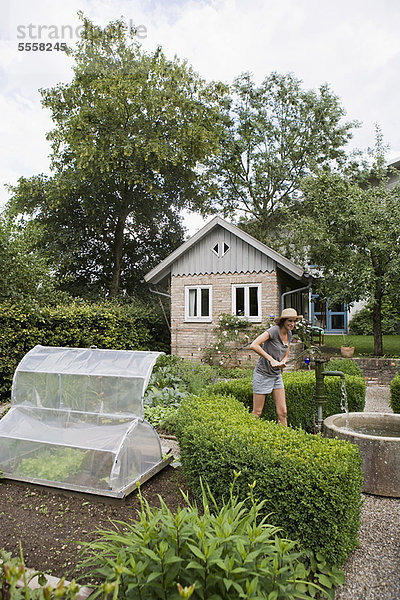 Lächelnde Frau beim Wasserpumpen im Garten