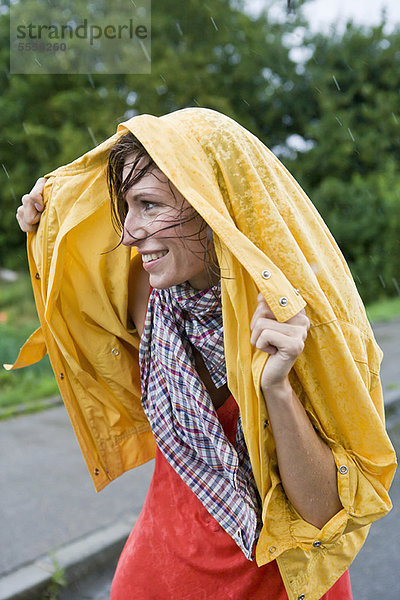 Lächelnde Frau bedeckt die Haare im Regen
