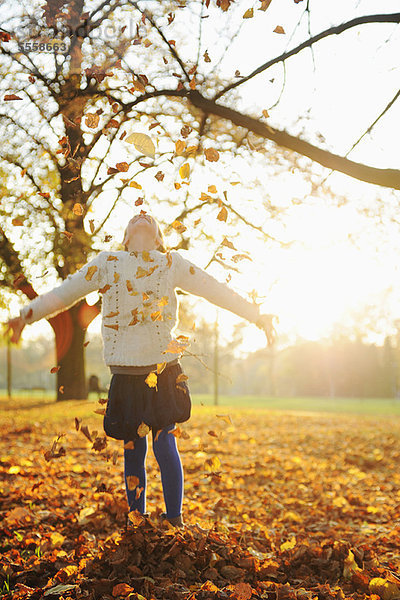 Lächelndes Mädchen spielt im Herbstlaub