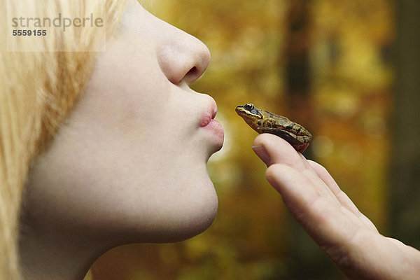 Mädchen küsst kleinen Frosch im Wald