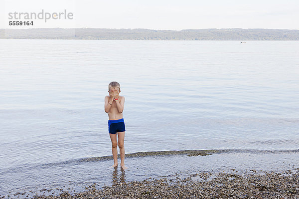Junge bedeckt sein Gesicht am Strand