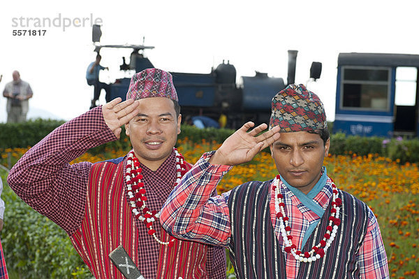 Zwei Nepalis in Tracht grüßen  dahinter die historische Eisenbahn  Darjeeling Himalayan Railway  Darjilingbahn  Schmalspurbahn  Toy Train  UNESCO Weltkulturerbe  Darjeeling  Westbengalen  Indien  Südasien  Asien