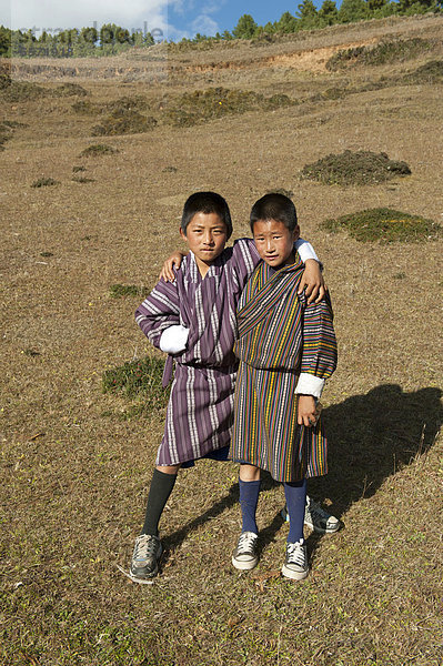 Zwei Jungs Arm in Arm auf Weide  Tracht  traditionelle Kleidung Gho  bei der Gangtey Goenba  Gangteng Kloster  Phobjika-Tal  Himalaja  Königreich Bhutan  Südasien  Asien