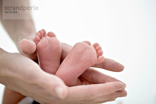 Hände eines Erwachsenen halten die Füße von einem Baby  1 Monat