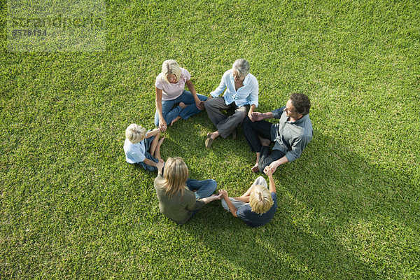 Menschen sitzen im Kreis auf Gras und halten sich an den Händen.