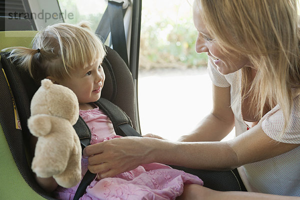 Mutter befestigt kleines Mädchen im Autositz