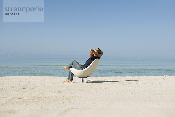 Mann im mittleren Erwachsenenalter entspannt im Sessel am Strand