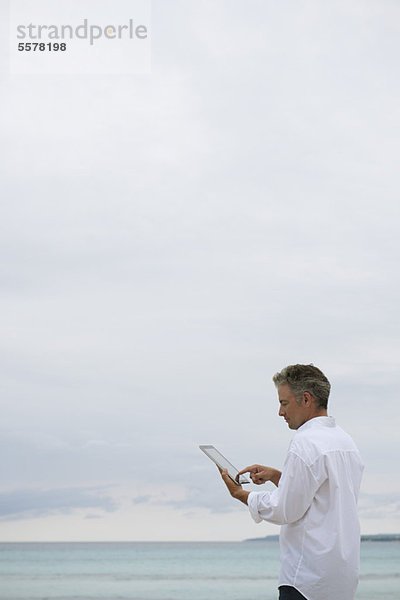 Der reife Mann mit digitalem Tablett am Meer