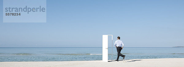 Mann läuft am Strand in Richtung offene Tür  Rückansicht