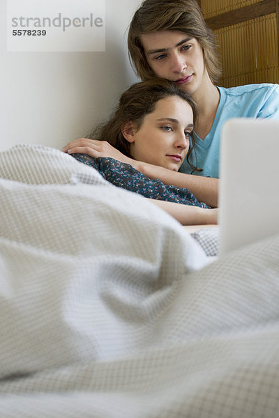 Junges Paar entspannt sich gemeinsam im Bett mit dem Laptop