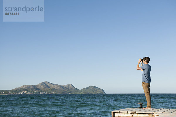 Mann am Pier stehend mit Blick auf das Meer durch ein Fernglas  Seitenansicht
