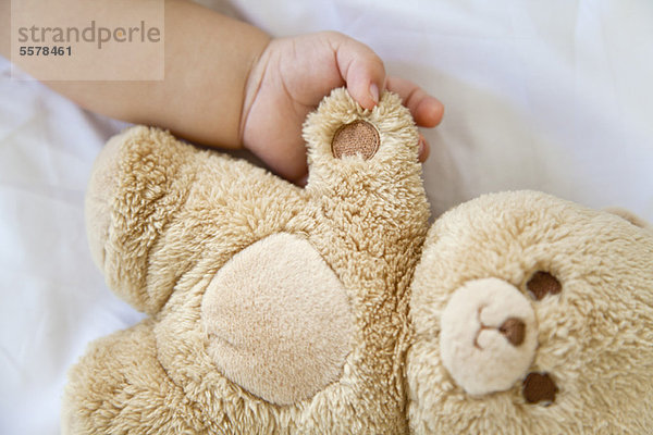 Baby hält Hände mit Teddybär  beschnitten