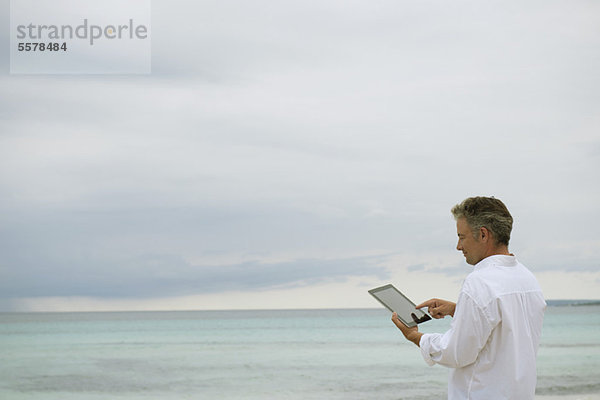 Der reife Mann mit digitalem Tablett am Meer