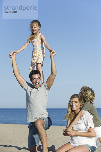 Familie spielt zusammen am Strand  Mädchen steht auf den Schultern ihres Vaters
