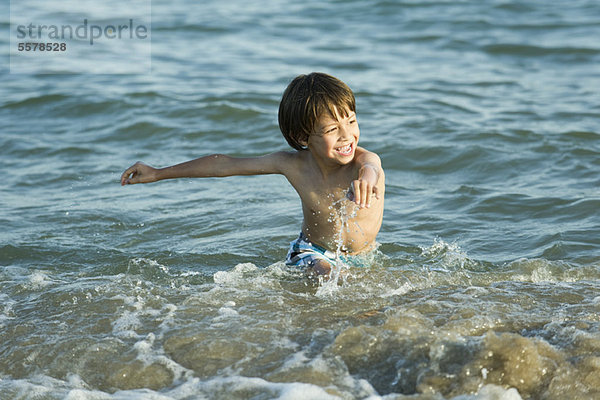 Junge spritzt im Wasser am Strand
