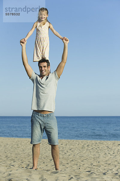Mädchen auf Vaters Schultern am Strand stehend
