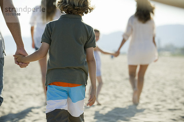 Junge am Strand mit seiner Familie  hält Vaters Hand  Rückansicht