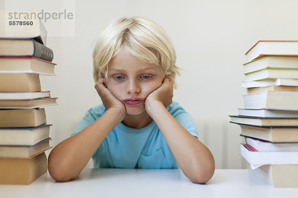 Junge sitzt zwischen zwei Stapeln von Büchern und schmollt.