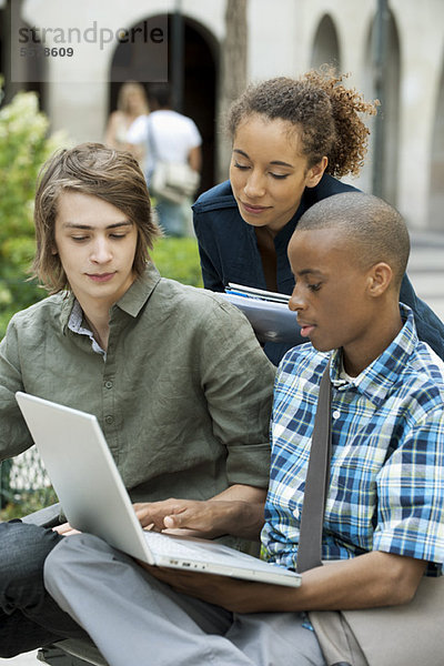 Studenten diskutieren Hausaufgaben auf dem Campus mit dem Laptop