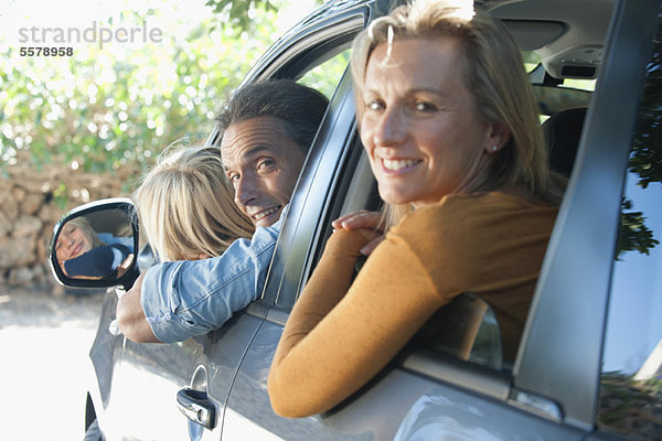 Familie zusammen im Auto  aus den Fenstern lehnend und über die Schultern lächelnd vor der Kamera.
