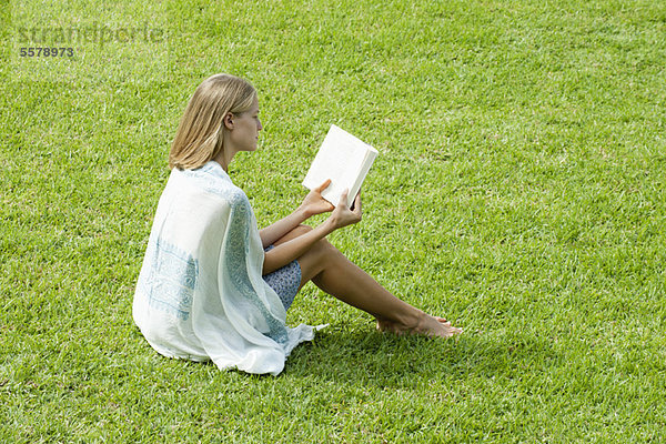 Junge Frau auf Gras sitzend Lesebuch