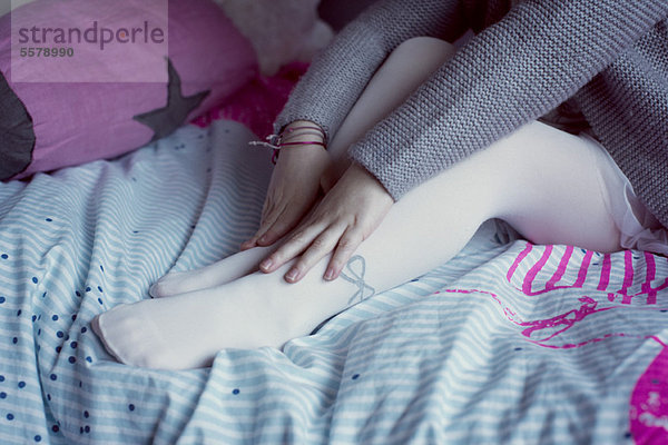 Kleines Mädchen auf dem Bett sitzend  Füße berührend  niedriger Abschnitt