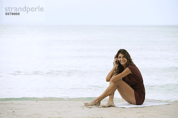 Junge Frau am Strand sitzend  mit Handy