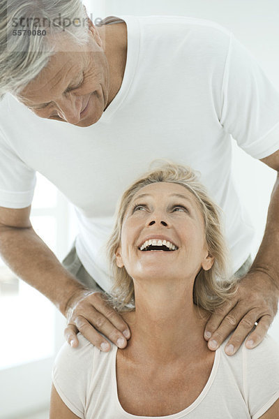 Ein reifes Paar lächelt sich an  während der Mann die Schultern der Frau massiert.