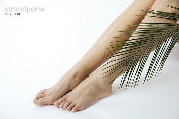 Frau hält Palmwedel an nackten Beinen  beschnitten