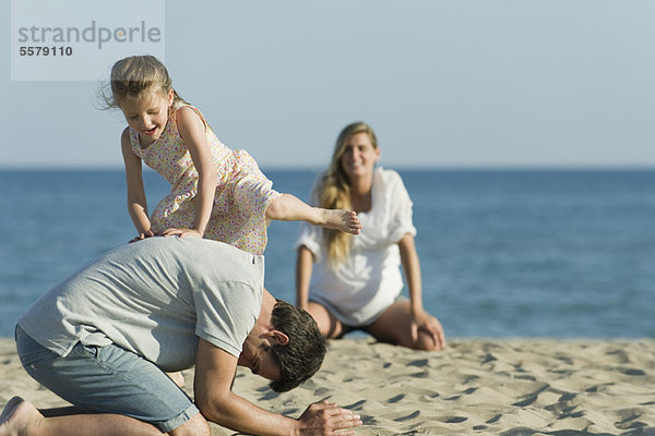 Mädchen spielt mit ihrem Vater am Strand