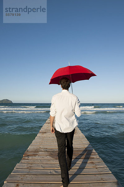 Mann auf Pier mit rotem Regenschirm  Rückansicht
