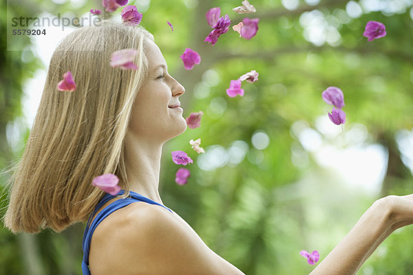 Junge Frau wirft Blütenblätter in die Luft  Seitenansicht