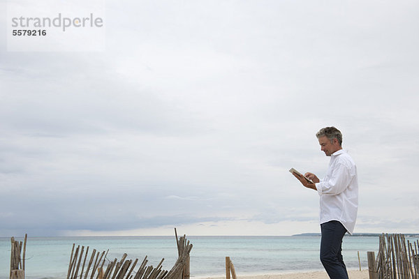 Erwachsener Mann mit digitalem Tablett am Strand
