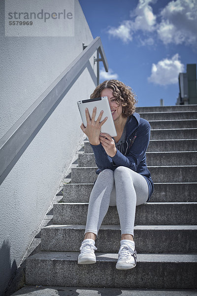 Frau sitzte mit Ipad auf einer Treppe