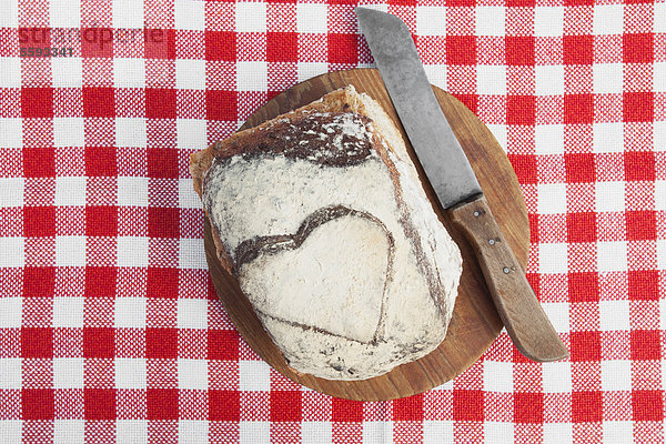 Brot mit Herzform auf Holzschneidebrett und Messer
