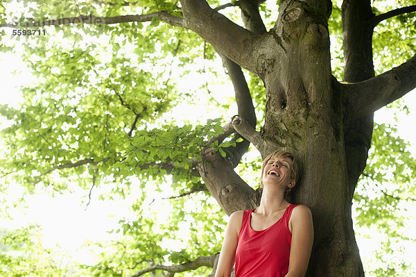 Mittlere erwachsene Frau  die sich auf einen Baum stützt  lächelnd