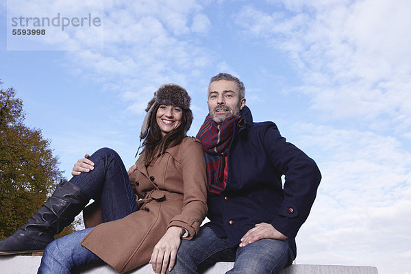 Deutschland  Köln  Paar auf Brücke sitzend  lächelnd  Portrait