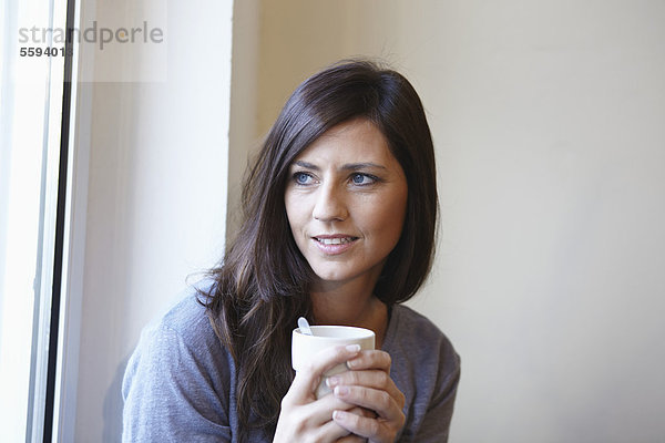 Mittlere erwachsene Frau am Fenster mit Kaffee  lächelnd