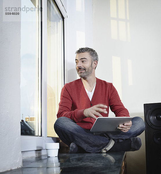 Erwachsener Mann am Fenster sitzend mit digitalem Tablett  lächelnd