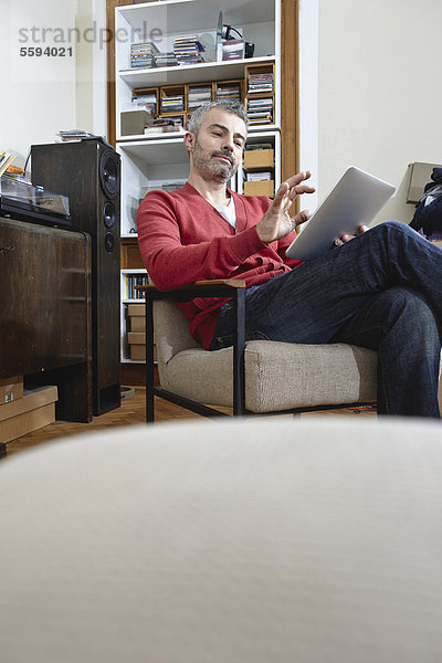 Erwachsener Mann sitzt auf Stuhl mit digitalem Tablett  lächelnd
