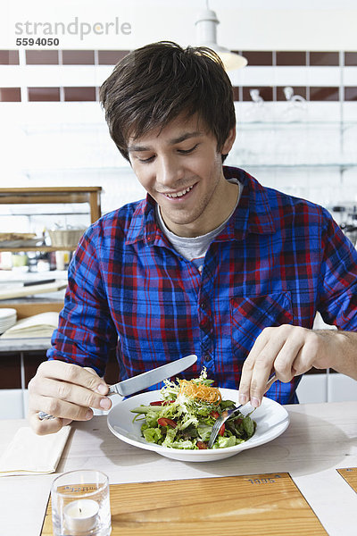 Junger Mann isst Salat  lächelnd