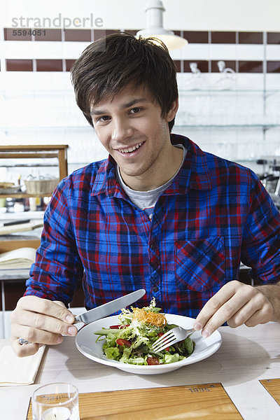 Junger Mann isst Salat  lächelnd  Porträt
