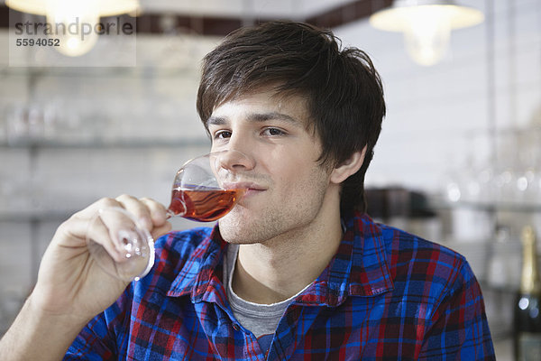 Junger Mann trinkt Wein  lächelnd